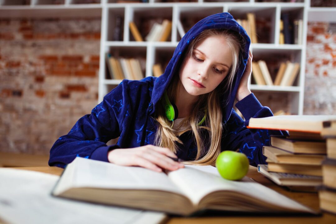 woman wearing blue jacket sitting on chair near table reading books